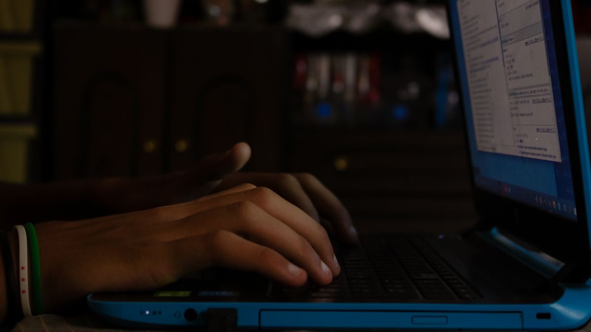 夜、暗い部屋でノートパソコンのキーボードを操作している手元のイメージ