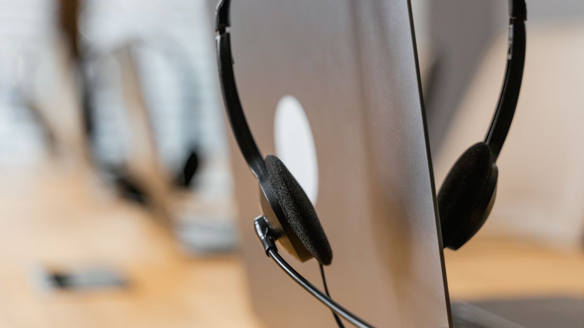 ノートパソコンに掛けられたマイク付きヘッドセットの接写。口元との距離が精度を左右することの比喩