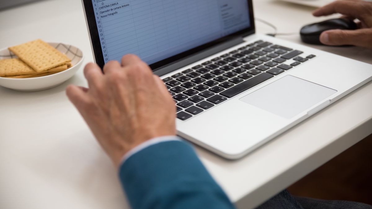 机の上のノートパソコンで表計算のシートを開き、キーボードとマウスに手を置いている様子