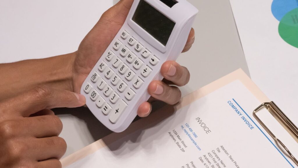 請求書の上で電卓を手に持ち、金額を確かめている手元