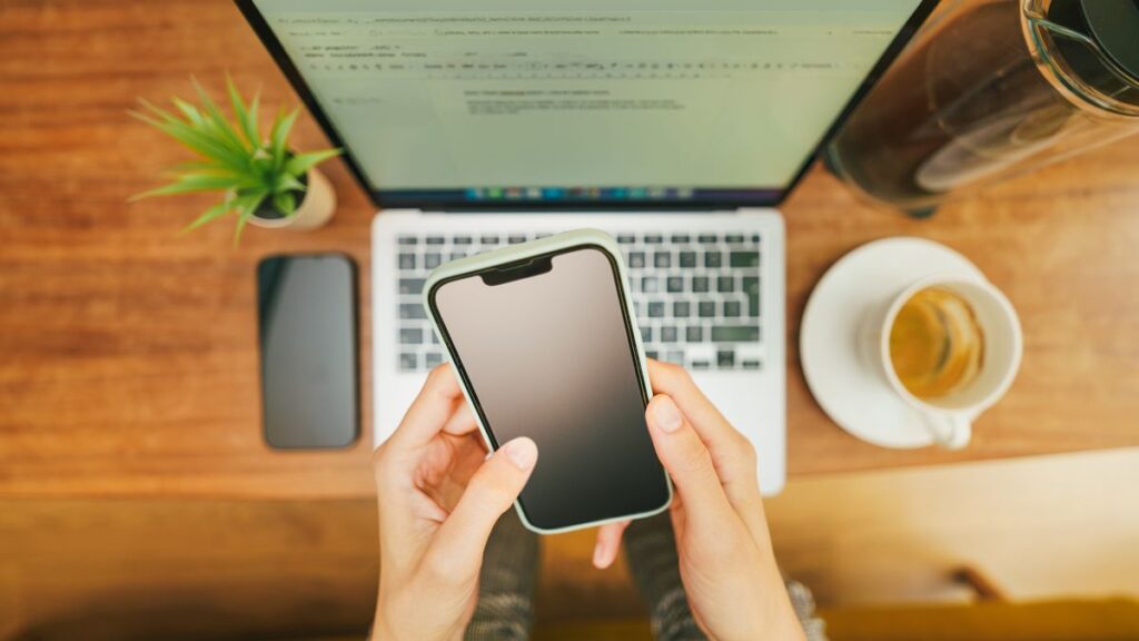 ノートパソコンの上でスマートフォンを操作する手元