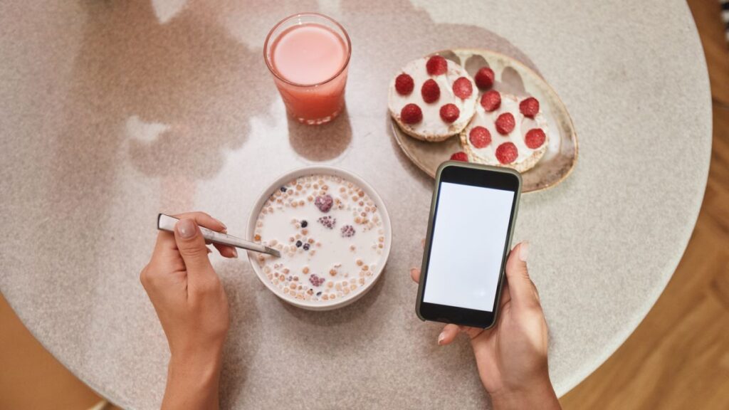 朝食のテーブルでスマホを持つ手。ChatGPTをスマホで始めるイメージ