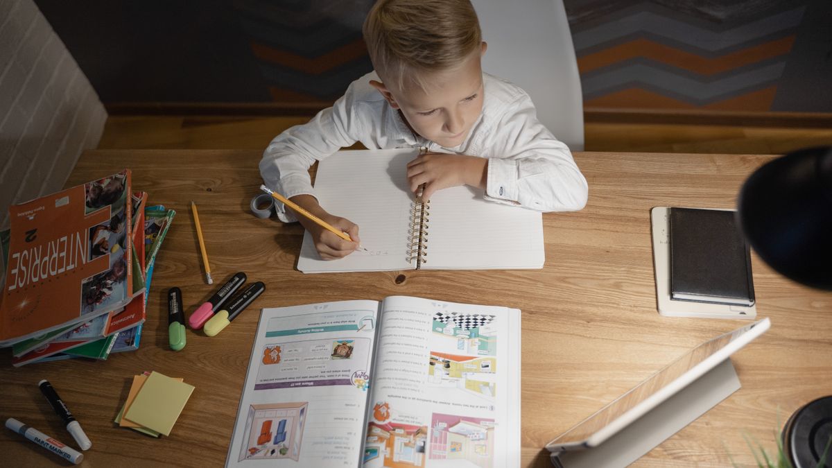 机で本とタブレットを広げて勉強する子ども