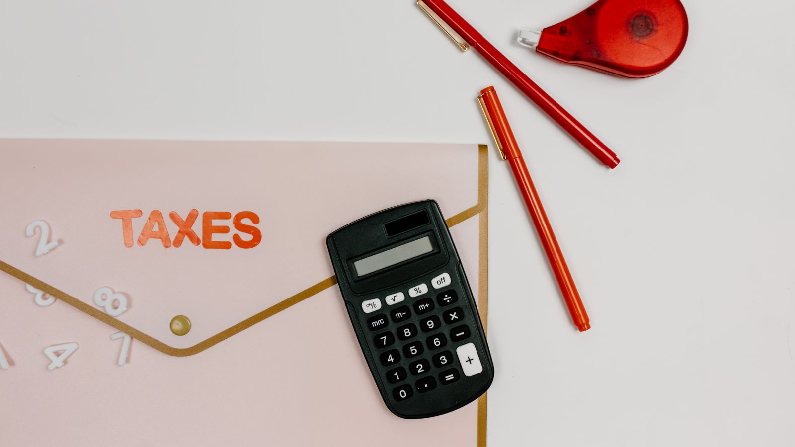 TAXESと書かれた書類ホルダーと電卓が並んだ机の上のイメージ