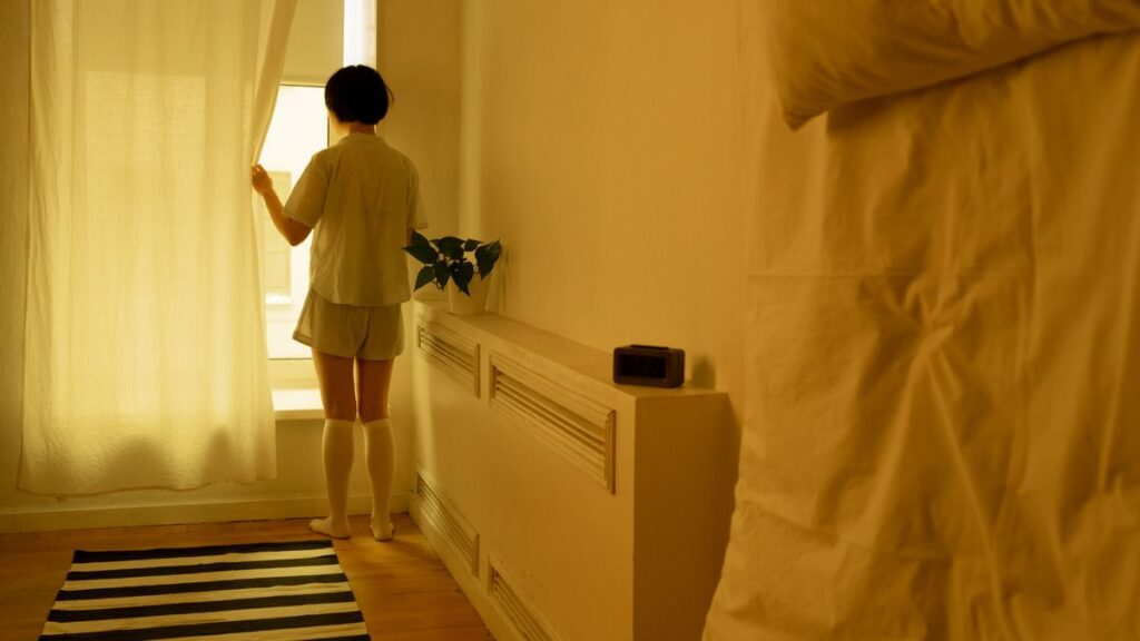 カーテンを開けて朝の光を部屋に入れている女性