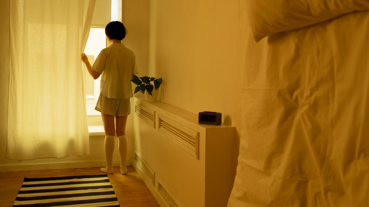 カーテンを開けて朝の光を部屋に入れている女性