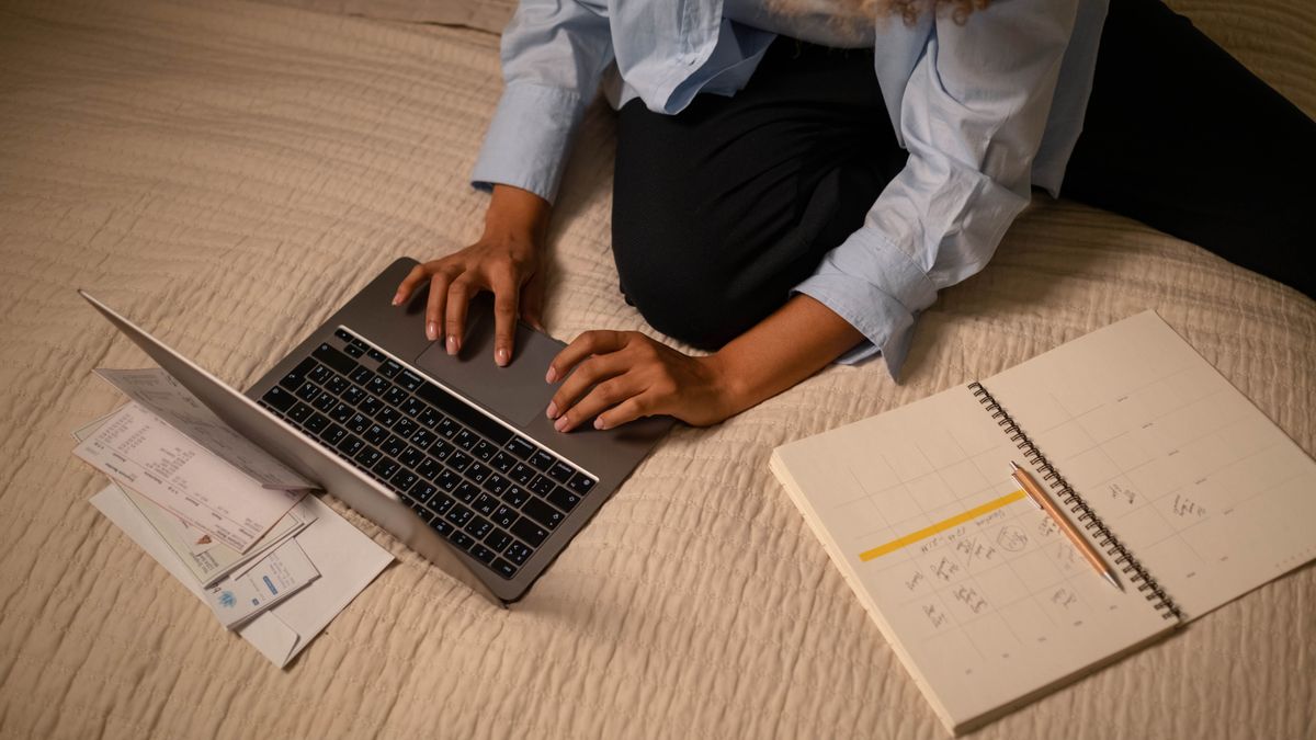 夜の部屋でノートパソコンと週間カレンダーを広げ、予定を書き込んでいる女性の手元