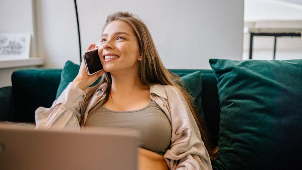ソファでくつろぎながら、笑顔でスマートフォンに向かって話している女性