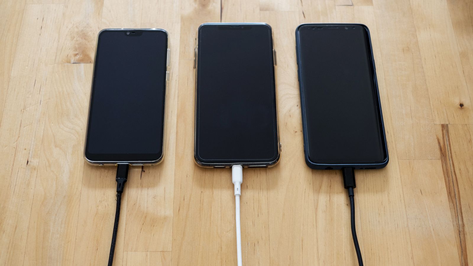 木の机に3台のスマートフォンが並んで充電されているイメージ