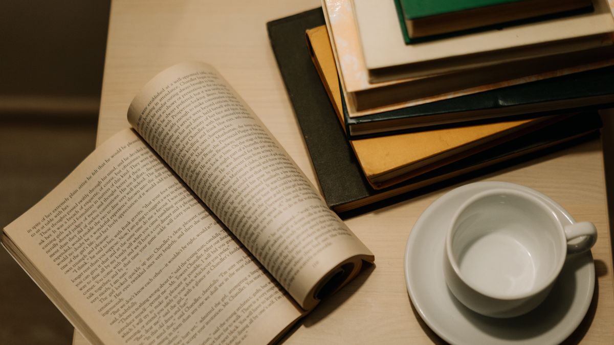 机の上に開かれた文庫本と積み重ねた本、白いコーヒーカップ。読書を習慣にするイメージ