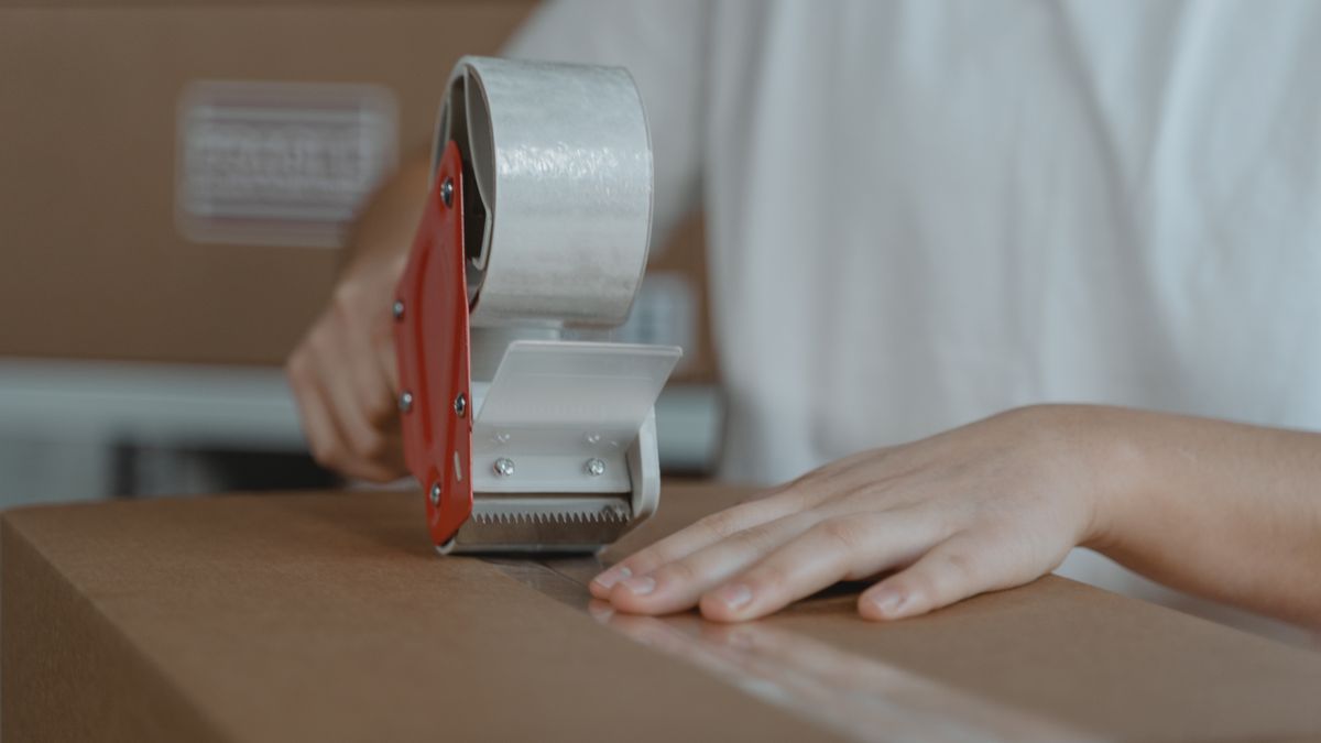 段ボール箱をテープで封をしている手元。自分で梱包して発送する物販のイメージ
