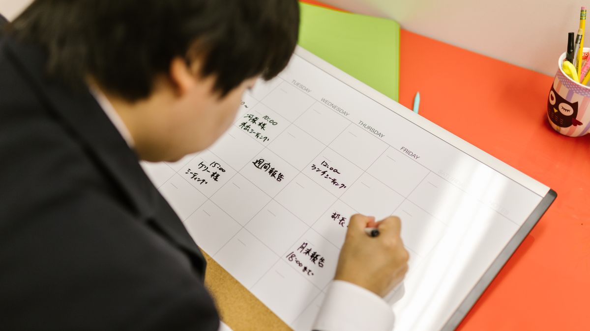 手帳に週の予定を書き込んでいる手元。予約枠を埋めていくイメージ
