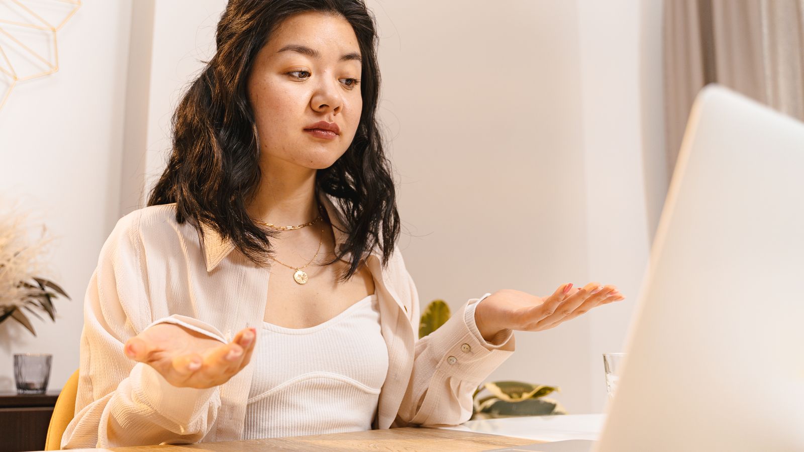 ノートパソコンの前で両手を広げ、腑に落ちない表情をしている人のイメージ
