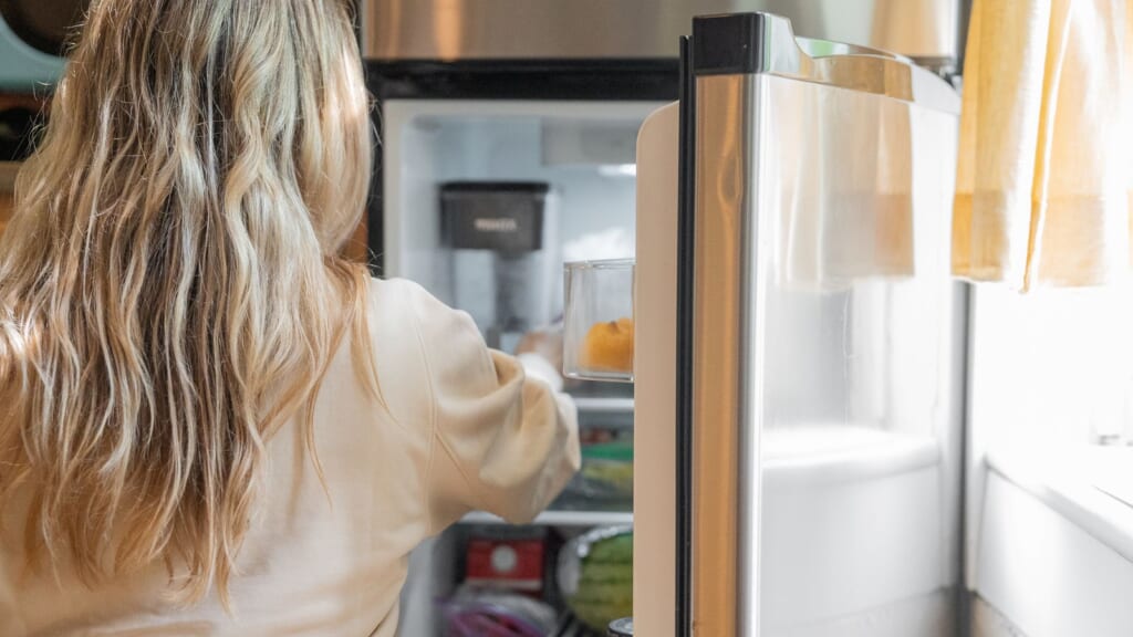 冷蔵庫を開けて中の食品に手を伸ばしている人の後ろ姿